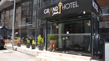 A hotel entrance with a glass facade, steps leading up to the door, and potted plants on the sidewalk.