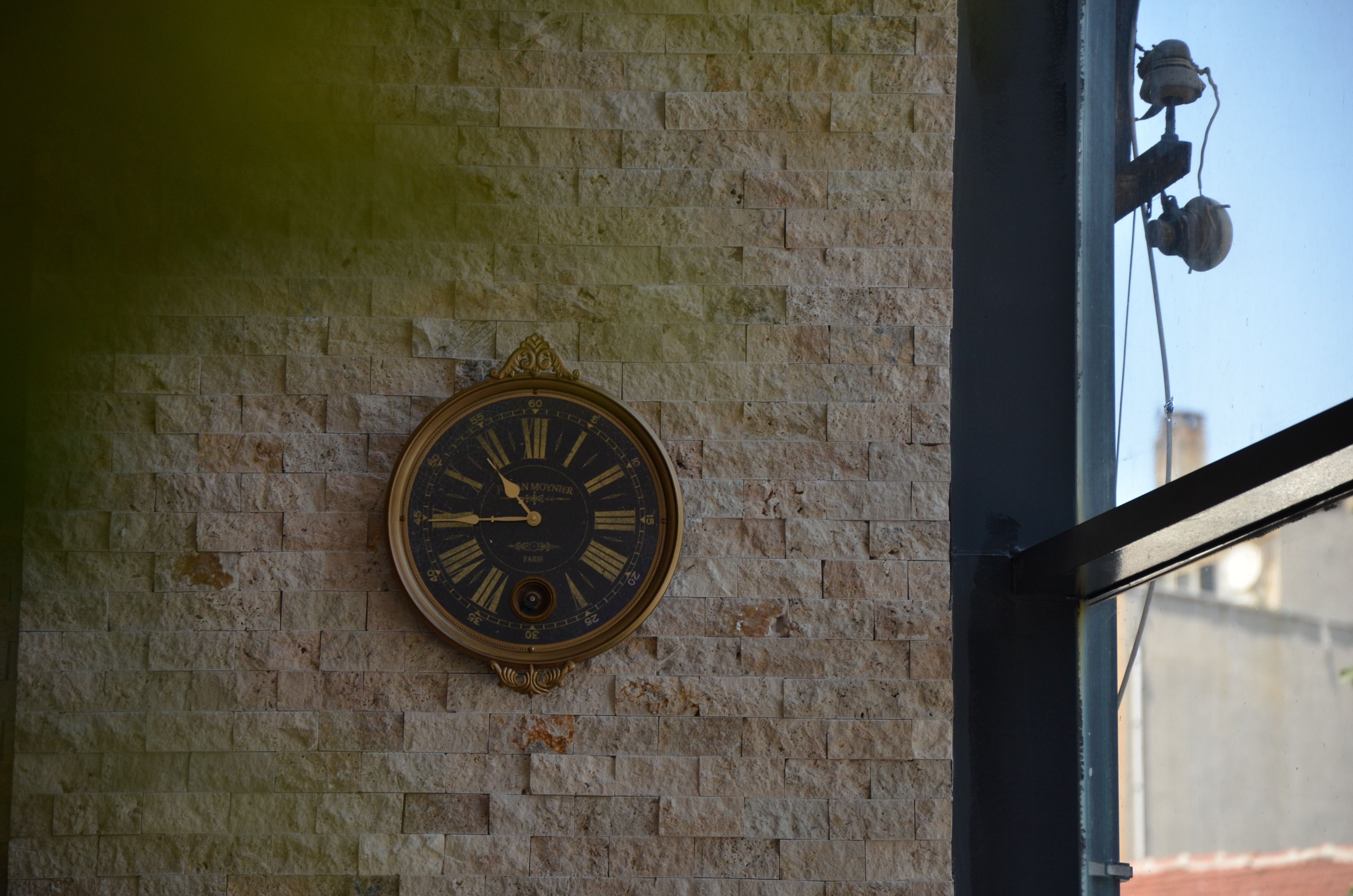 Un reloj de pared con números romanos y un péndulo, sobre un muro de ladrillo texturizado.