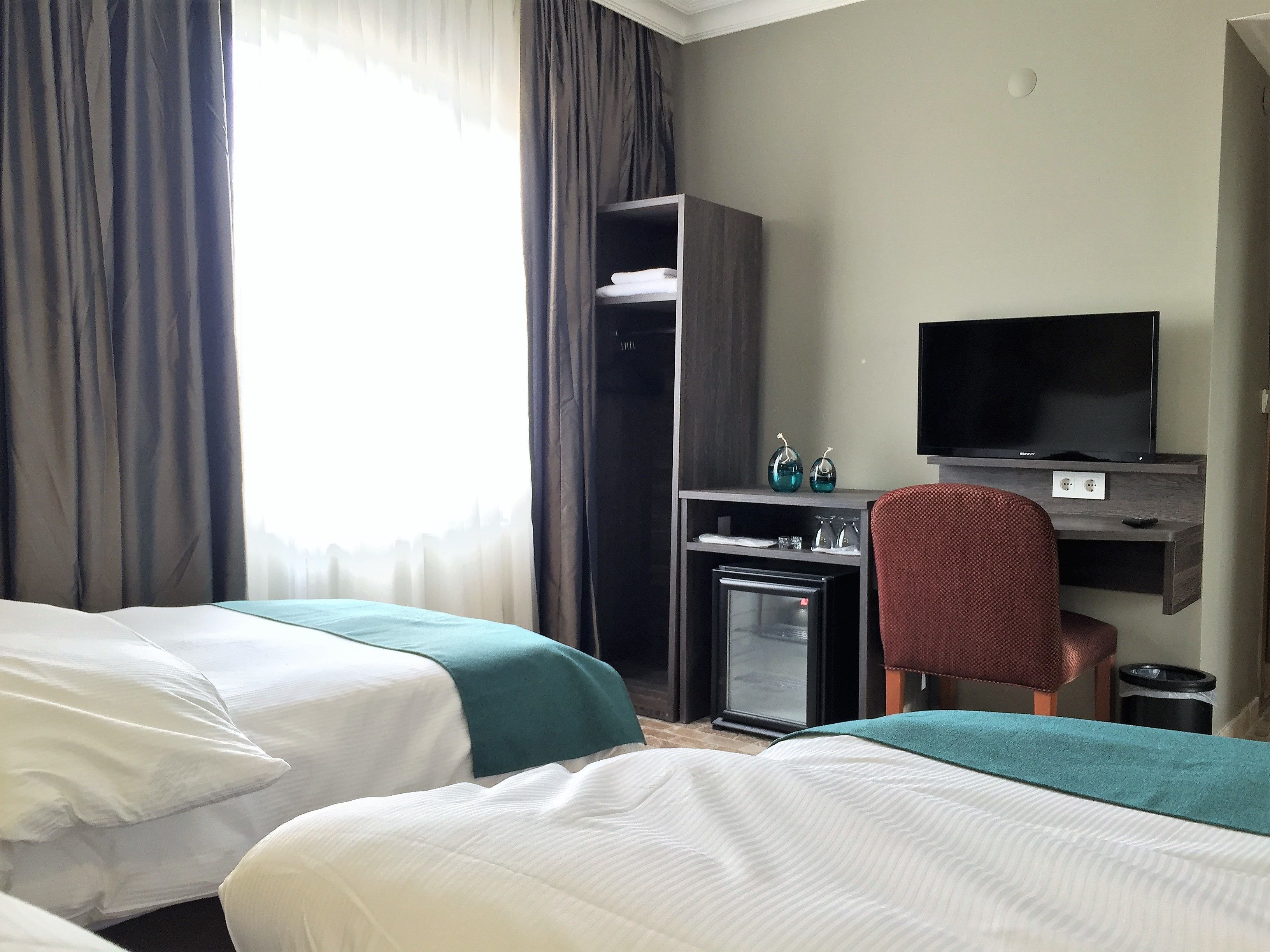 Habitación de hotel con dos camas, un escritorio con televisor, un refrigerador pequeño y una silla.