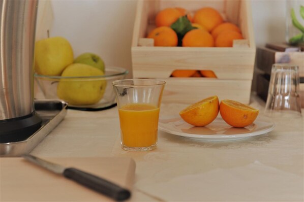 A kitchen counter with a glass of orange juice, a plate with two halves of an orange, a fruit bowl with apples and oranges, and a salt shaker. - Hotel Peschici (Peschici)