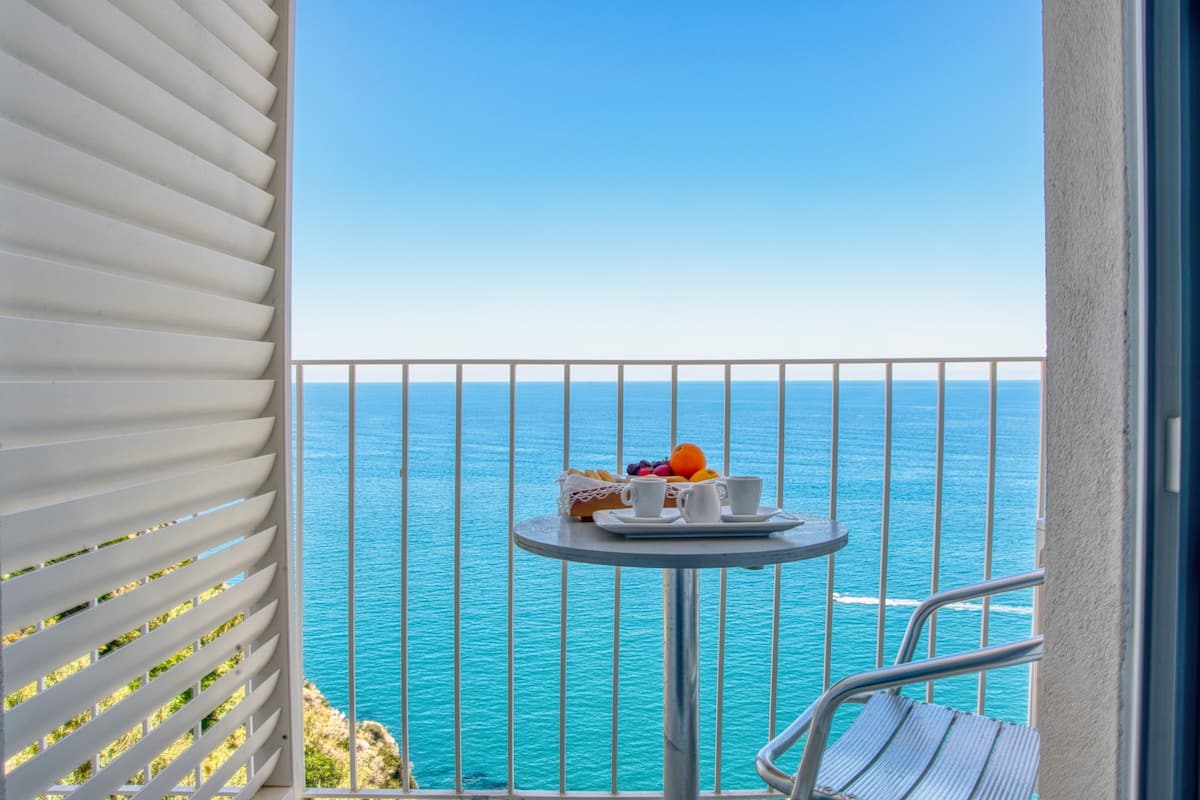 Un balcón con una mesa dispuesta para el desayuno, con vista a un mar azul y despejado.