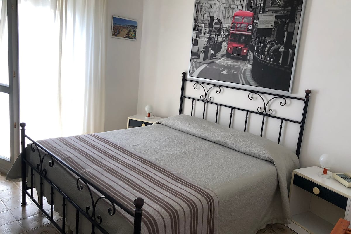 Un dormitorio con cama, una mesita de noche, una lámpara de pared y un cartel de un autobús rojo de dos pisos.
