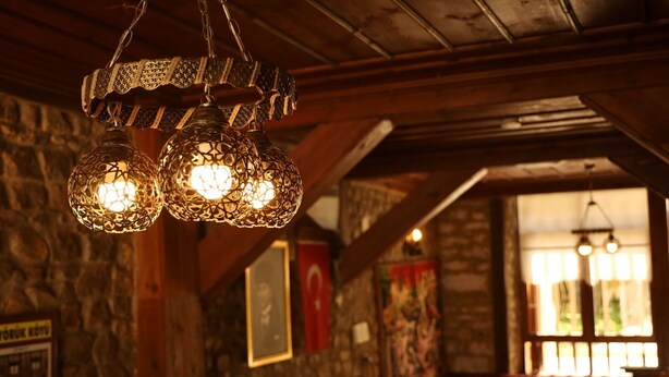 A rustic interior with exposed wooden beams, stone walls, and hanging metal light fixtures.