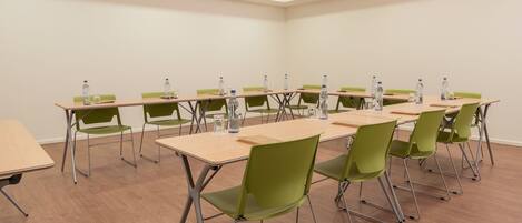 Une salle de conférence dotée de plusieurs tables et chaises, ainsi que de bouteilles d’eau et de carnets.