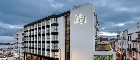 Um hotel moderno com um letreiro chamativo que diz 'neat', fachada limpa, janelas amplas e uma loja de esquina.