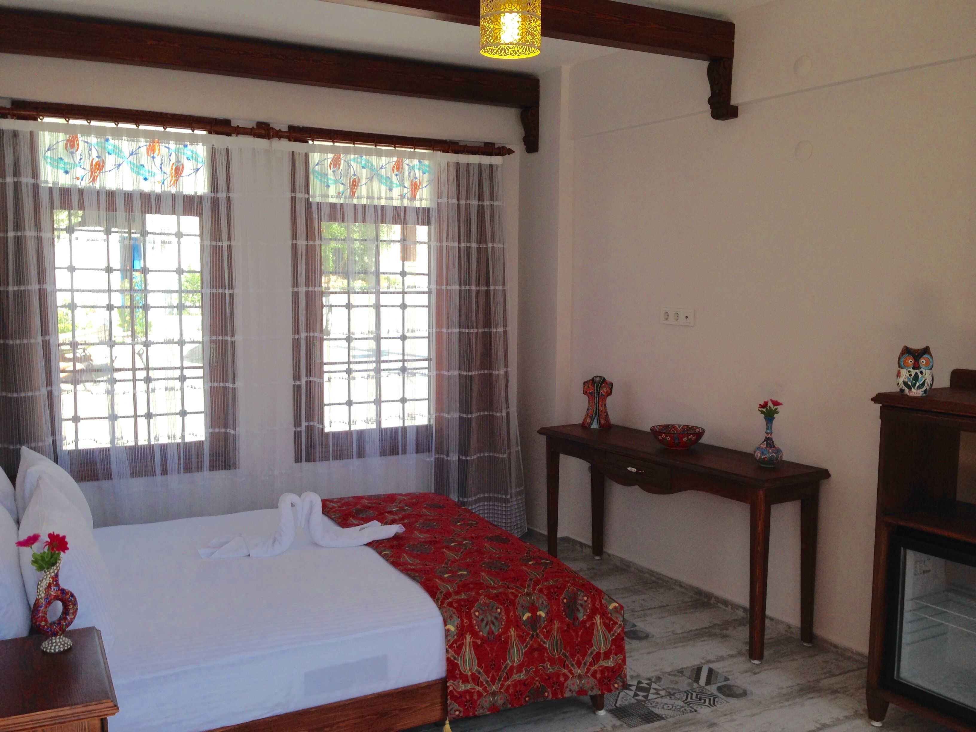 A hotel room with a bed, a wooden nightstand, a table with a vase, and a television.