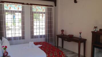 A hotel room with a bed, a wooden nightstand, a table with a vase, and a television.