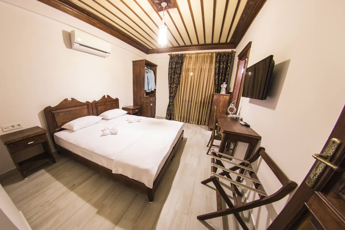A bedroom with a wooden bed, a nightstand, a desk with a chair, a mirror, and a TV on the wall.