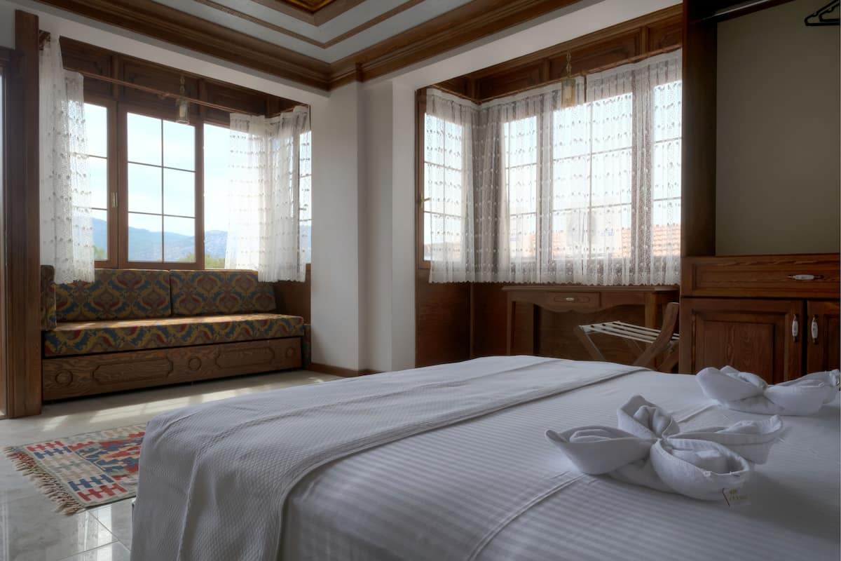 A hotel room with a large bed, a sofa, a wooden cabinet, and a window with curtains.