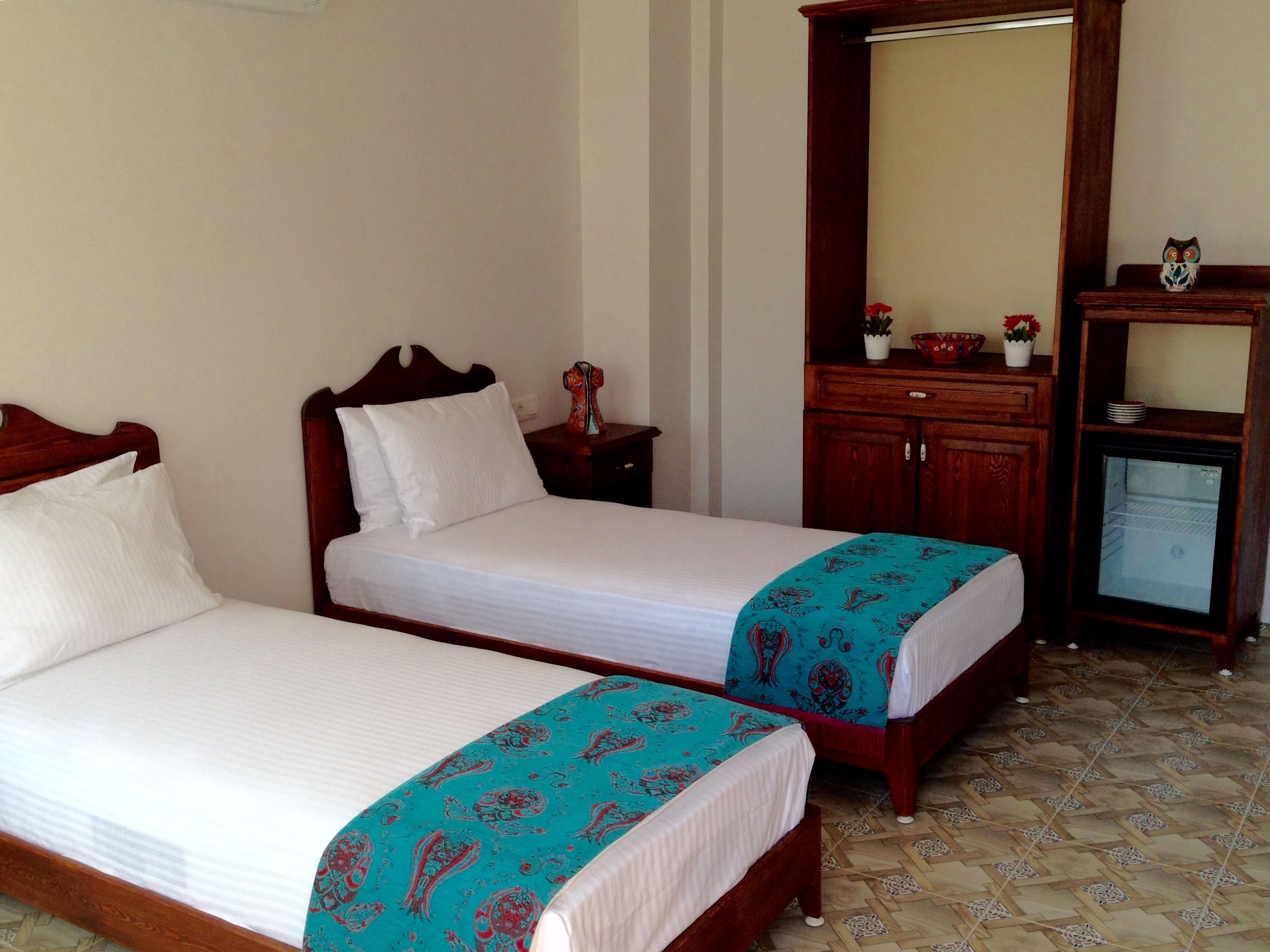 Een hotelkamer met twee eenpersoonsbedden, een houten dressoir, een spiegel en een kleine koelkast.