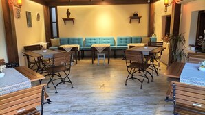 A cozy dining area with wooden tables and benches, a teal cushioned bench in the center, and wall-mounted shelves with decorative items. - Hotel Mary's House (Selçuk)