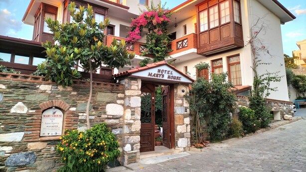 Un hotel de dos pisos con fachada de piedra, un balcón con barandillas de madera y un letrero que dice "Hotel Mary's House".
