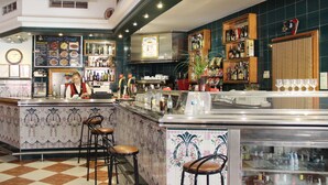 A bar area with a tiled floor, bar stools, a counter with a menu, and shelves with bottles. - Hotel Teruel (Vinaros)