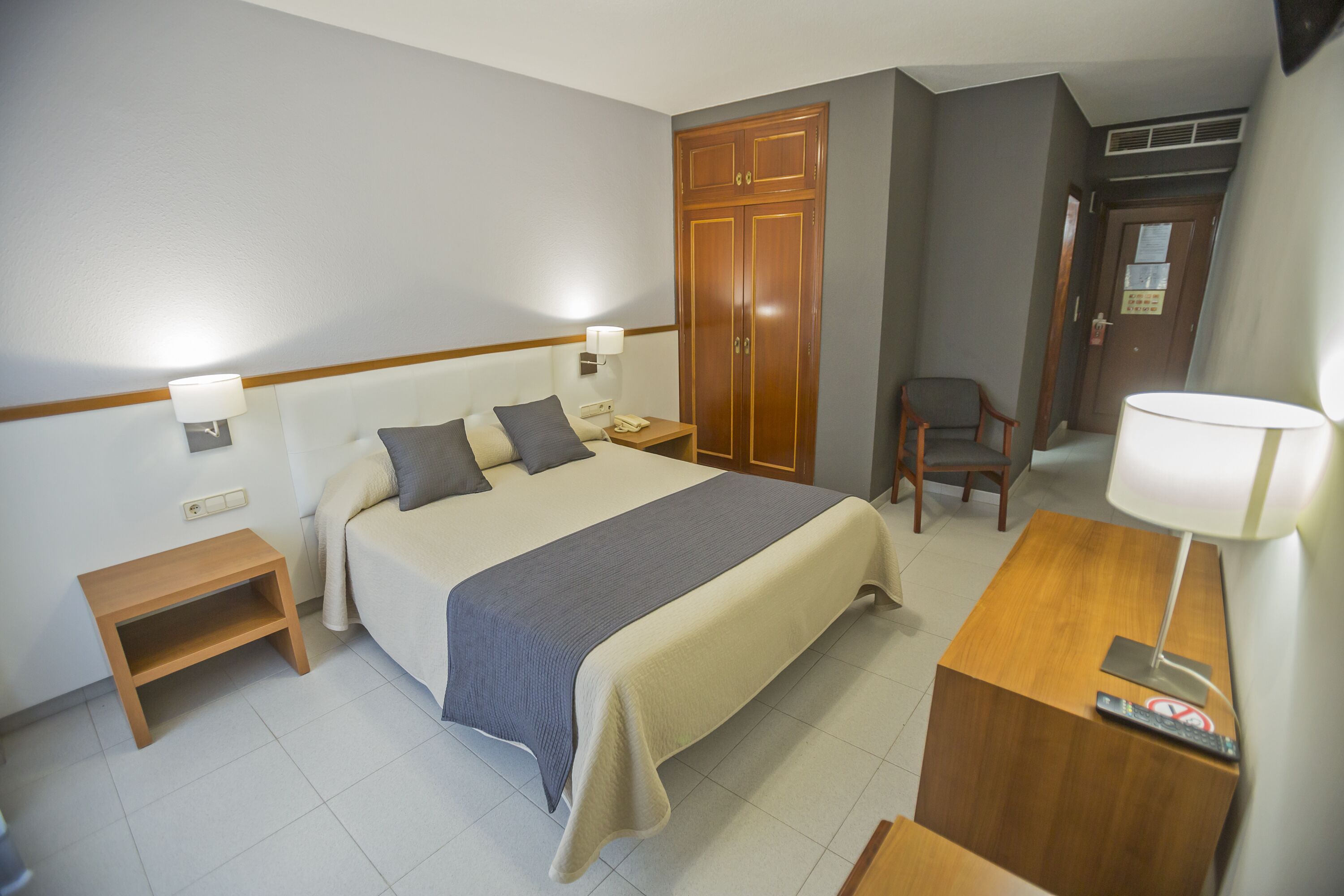 Habitación de hotel con cama, mesitas de noche, escritorio con lámpara, una silla y armario.