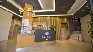 A hotel reception area with a reception desk, information stand, and a staircase leading to the service area. - Hotel Teruel (Vinaros)