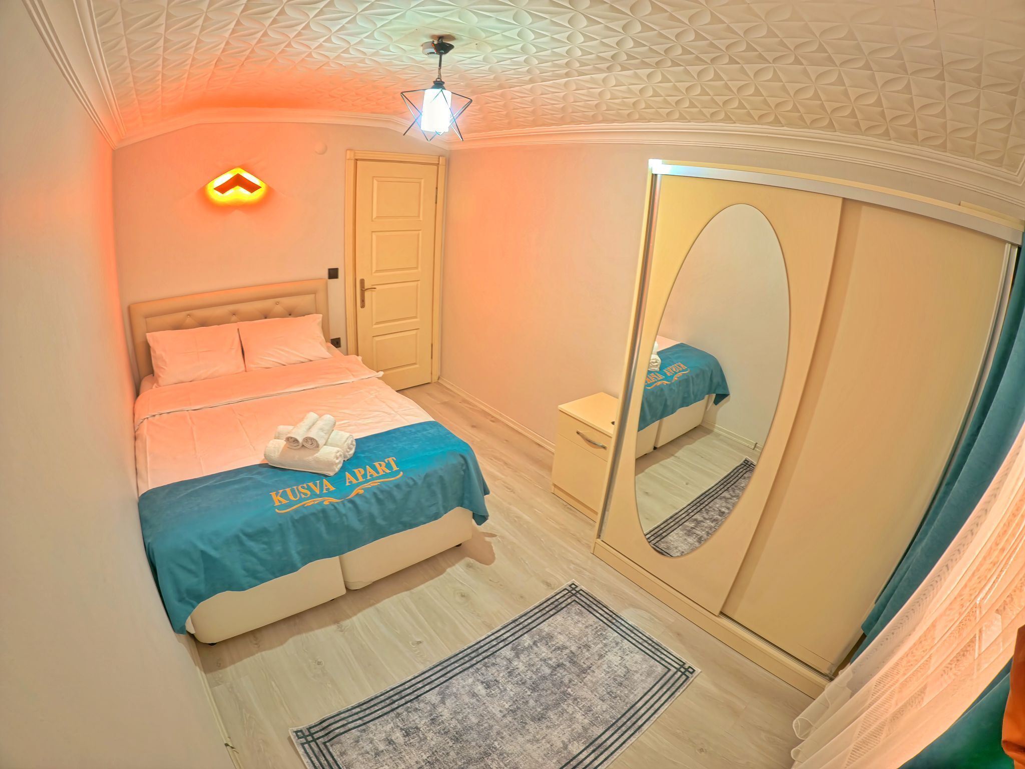 A bedroom with a bed, a wardrobe, a mirror, and a ceiling light.