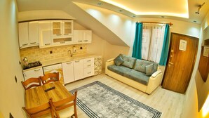 A compact living space with a kitchenette, a sofa, a dining table with chairs, and a patterned rug. - Uzungol Kusva Apart (Çaykara)