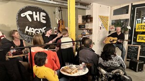 A group of people seated at tables in a casual dining setting with a musician performing. - The Golden Stork - Hostel (The Hague)