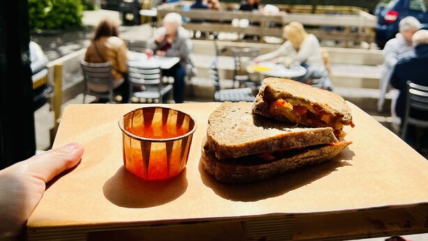 A wooden tray with a sandwich and a glass of orange juice on a table. - The Golden Stork - Hostel (The Hague)