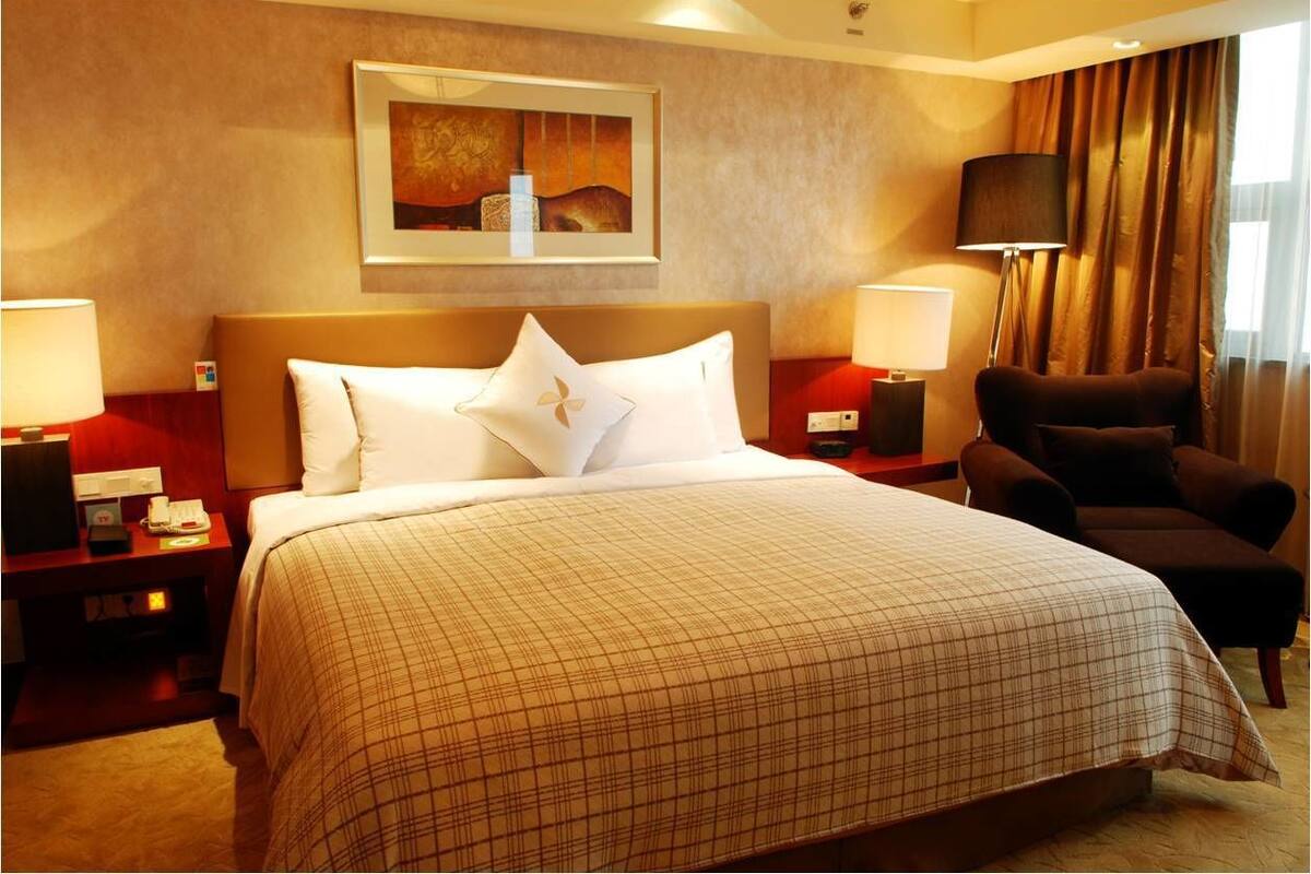 Una habitación de hotel con una cama grande, dos mesitas de noche, una silla, un cuadro en la pared y una lámpara.