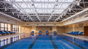 Una piscina interior con baldosas azules, múltiples carriles y sillas reclinables azules a los lados.