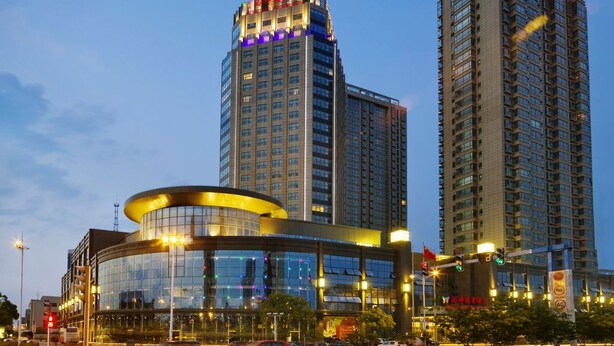 Un hotel moderno con fachada de vidrio curva, rodeado de edificios altos.