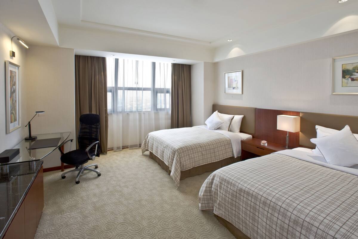 Habitación de hotel con dos camas, un escritorio con silla, televisión y ventana con cortinas.