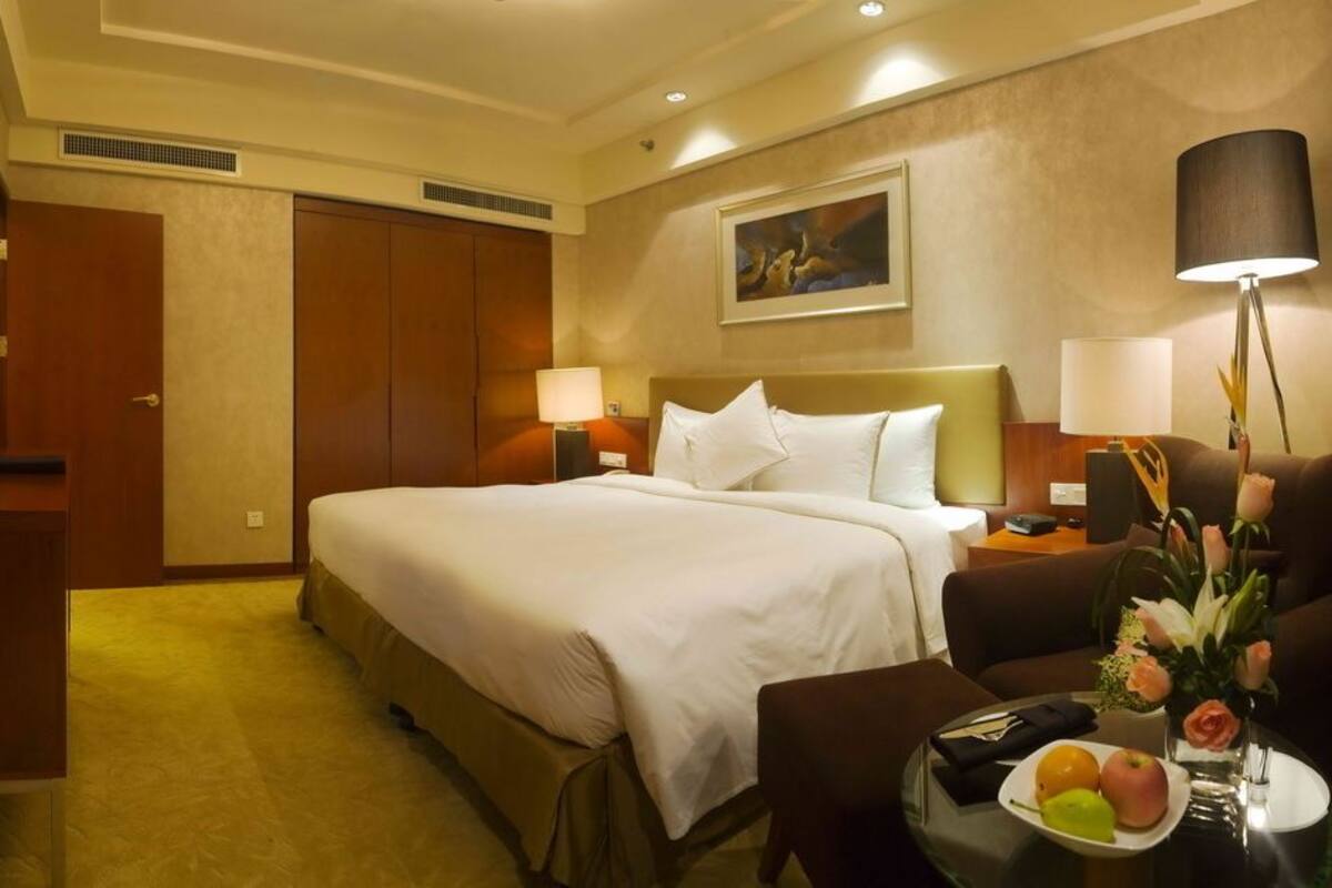 Habitación de hotel con una cama grande, un escritorio, una silla, un televisor y una mesa con fruta y flores.