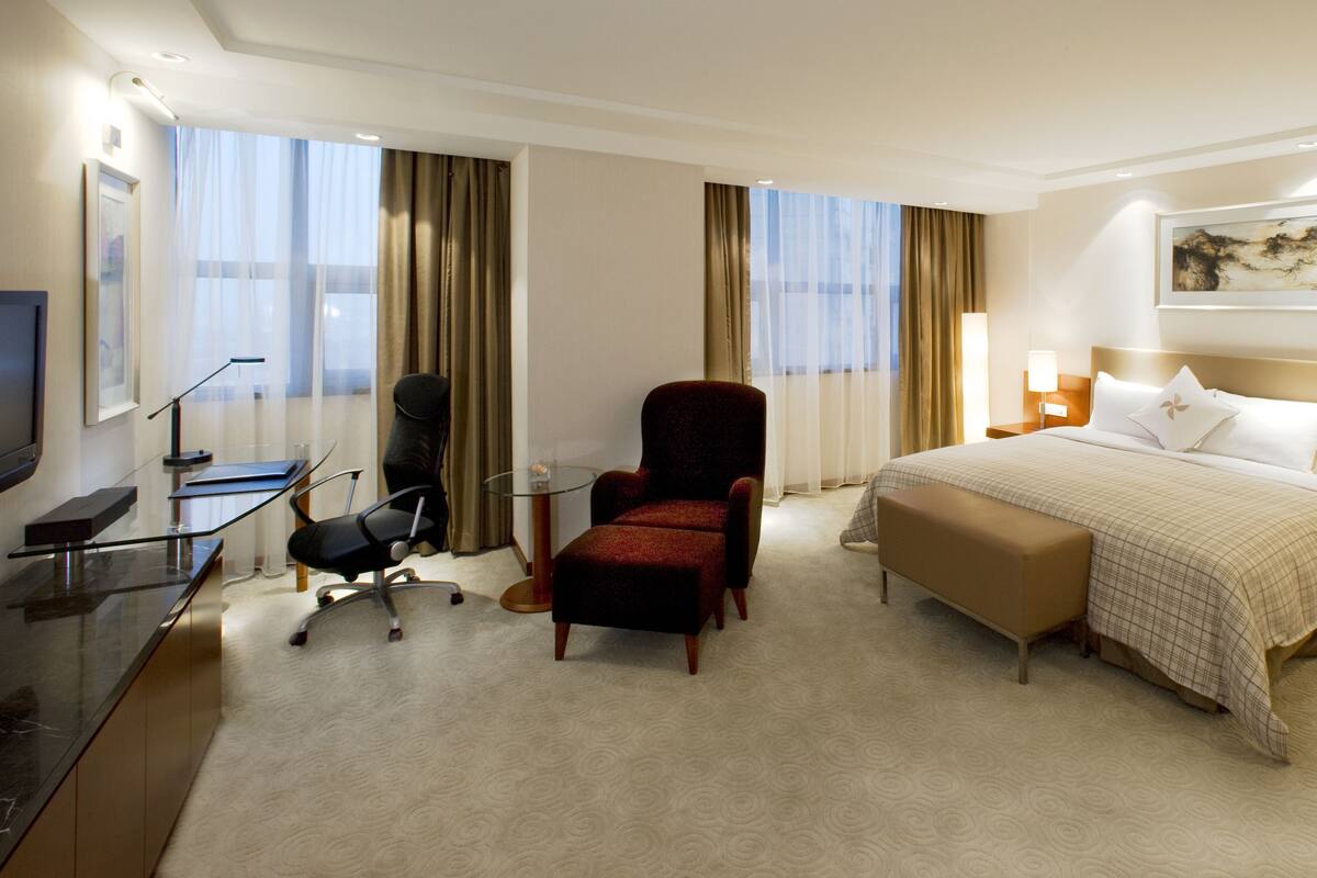 Habitación de hotel con cama, escritorio, silla, televisión y ventana con cortinas.