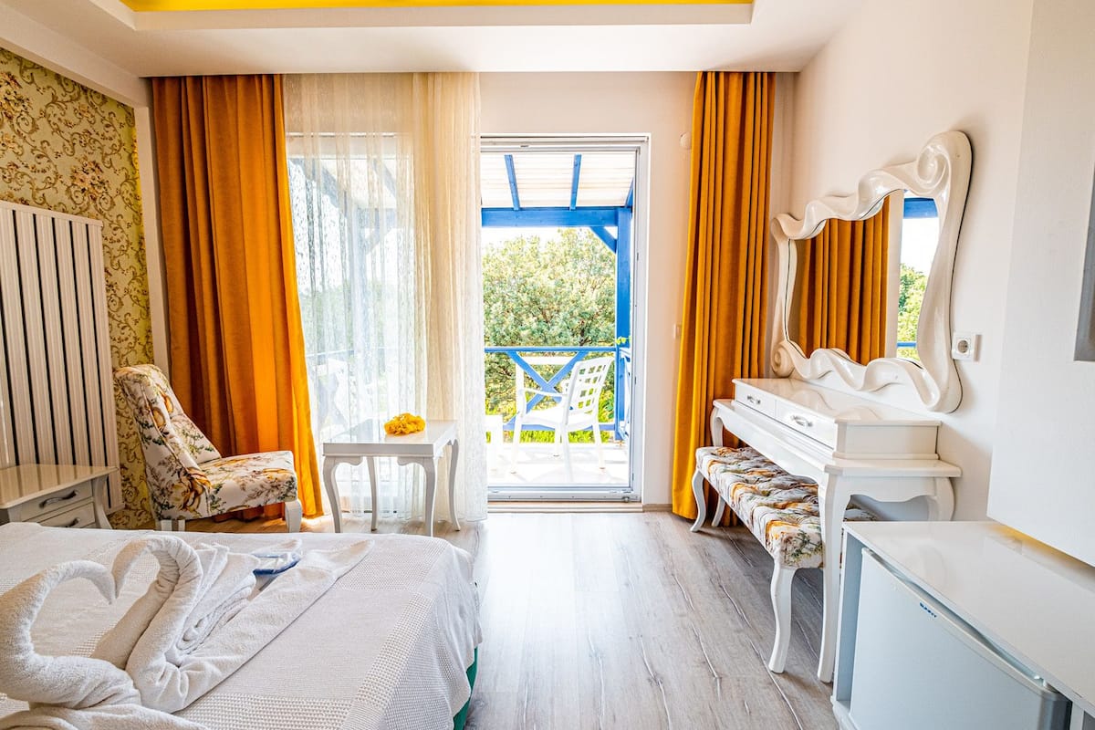 Hotelkamer met een bed, een bureau, een stoel, een klein tafeltje en een balkon met een blauwe reling.