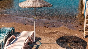 Une plage avec une terrasse en bois, des chaises longues, un parasol et une jetée qui s’avance dans l’eau.
