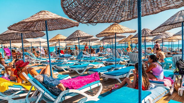 Un espace de détente aménagé sur la plage, avec plusieurs chaises longues et des parasols en feuilles de palmier.
