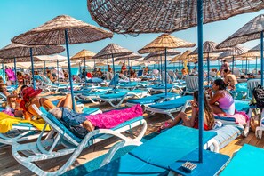 Un área de descanso en la playa con múltiples tumbonas y sombrillas de paja.