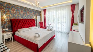 Une chambre moderne avec un lit recouvert d’un tissu rouge, un papier peint à motifs, un lustre et une vue sur l’extérieur grâce à de grandes fenêtres.