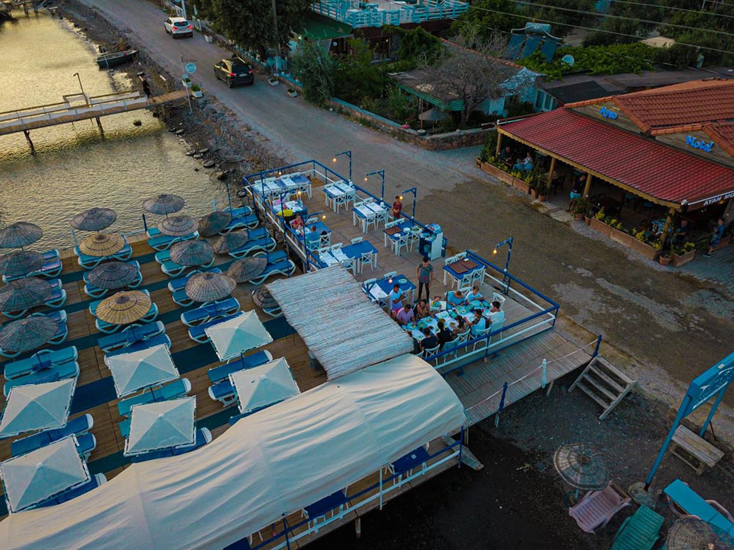 Un restaurante frente al agua con terraza, una zona techada y un edificio con tejado rojo.