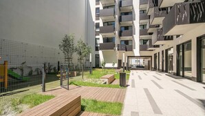 Edificio de apartamentos moderno con un patio que cuenta con bancos de madera, un parque infantil y un área cercada.