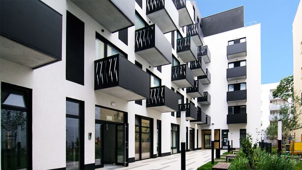 Un edificio moderno con balcones, ventanas amplias y un patio con bancos y follaje.