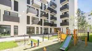 Un parque infantil con toboganes y estructuras para escalar, rodeado por un moderno edificio de apartamentos con balcones.