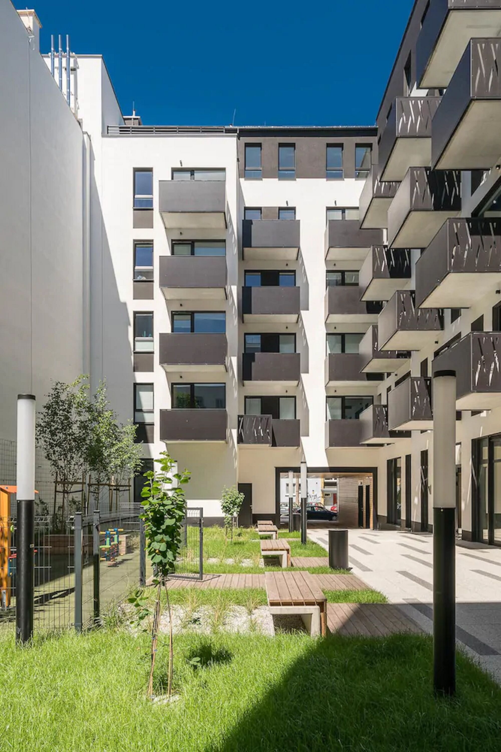 Un moderno edificio de apartamentos con varios balcones, un patio con césped y mobiliario exterior.
