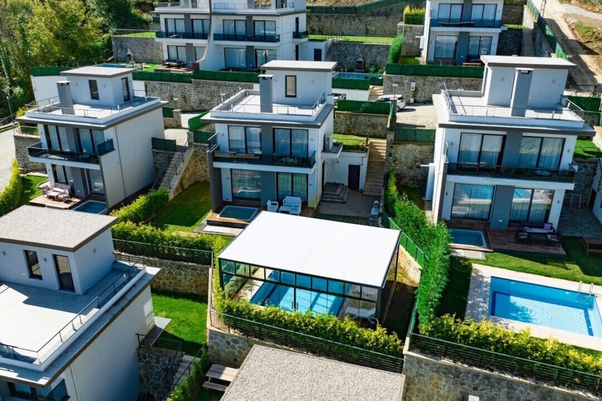 Ein moderner Wohnkomplex mit mehreren zweistöckigen Häusern, jedes mit großen Fenstern, Balkonen und einem Swimmingpool.