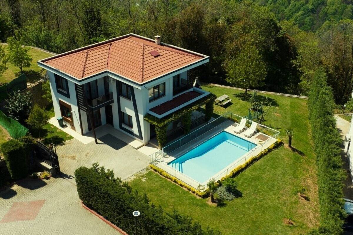 Ein modernes, zweistöckiges Haus mit Swimmingpool, umgeben von üppiger Vegetation und Hügeln.