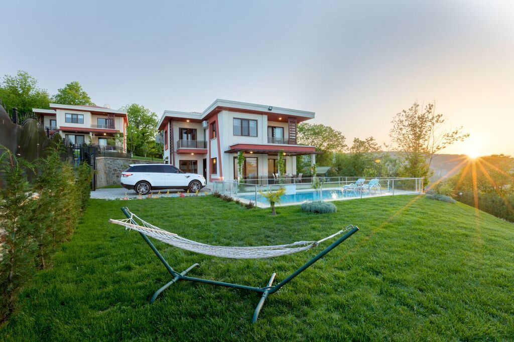A modern two-story house with a swimming pool, a hammock, and a parked car.