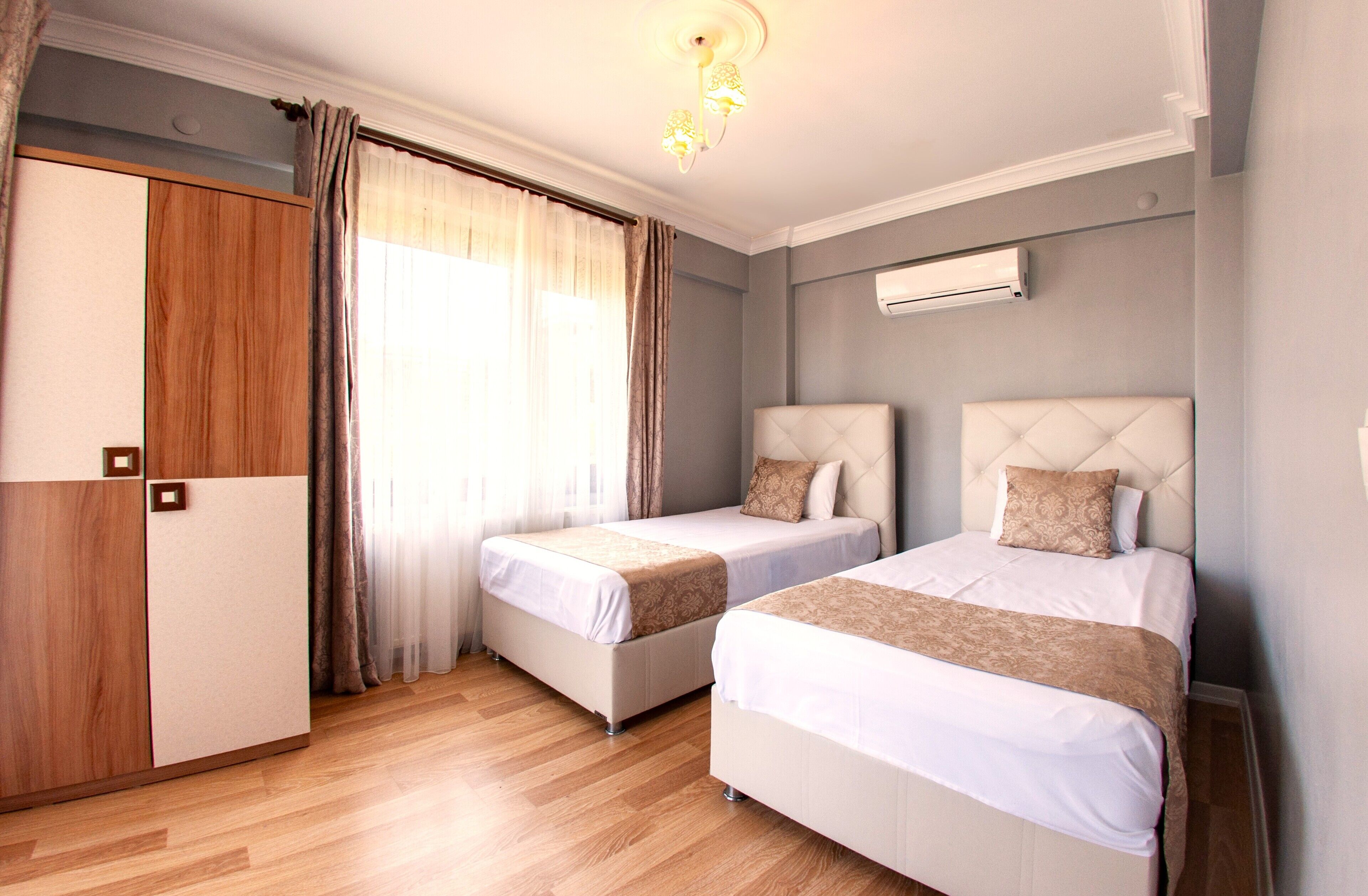 A hotel room with two beds, a wardrobe, and an air conditioning unit.