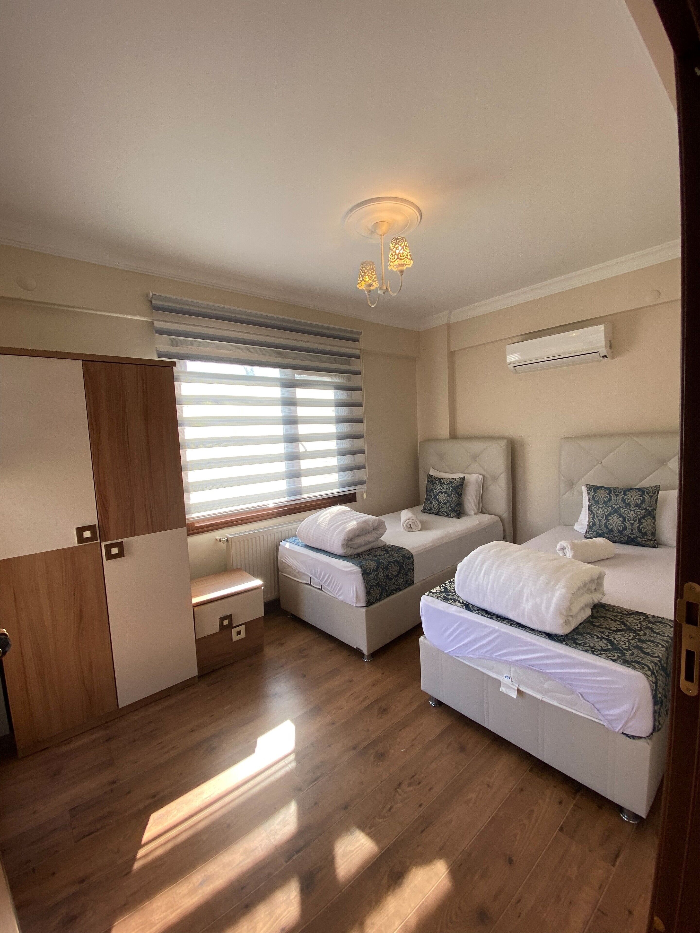 Een slaapkamer met twee bedden, een kledingkast, een radiator en een raam met zonwering.