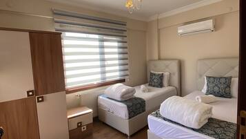 Een slaapkamer met twee bedden, een kledingkast, een radiator en een raam met zonwering.