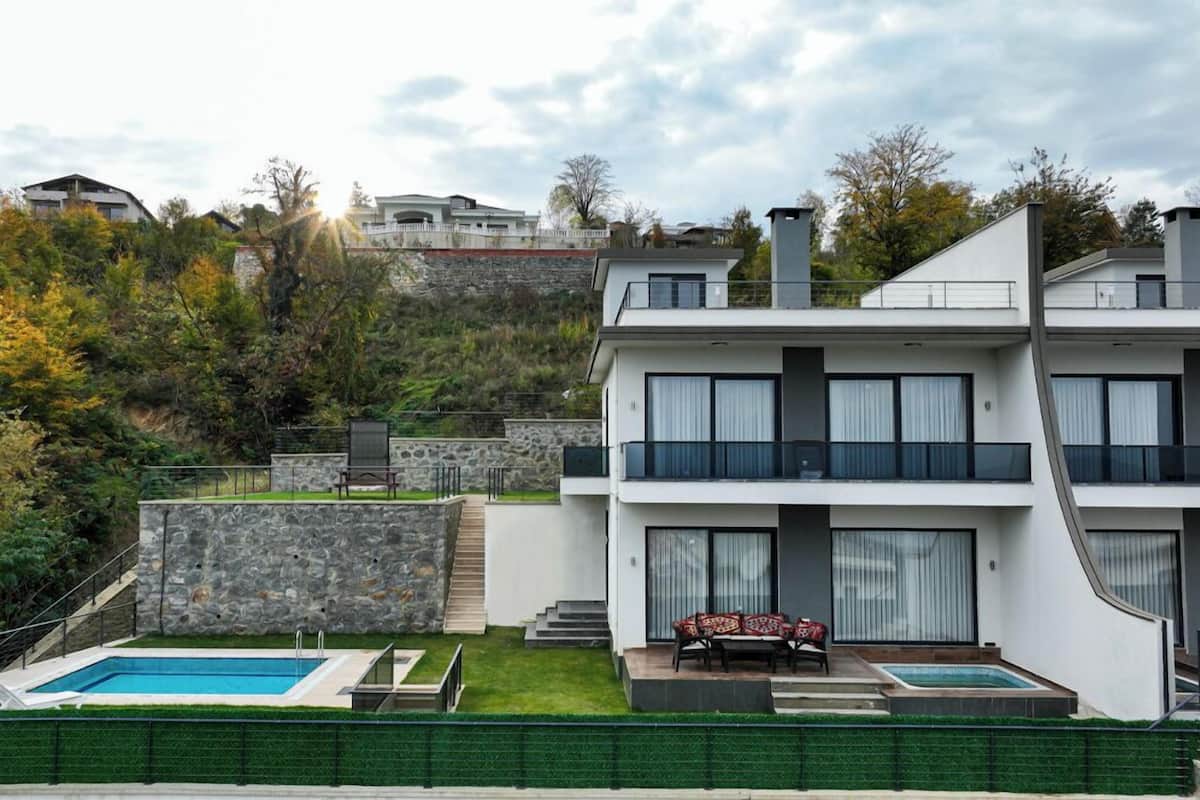 Ein modernes, zweistöckiges Haus mit Swimmingpool, einer Steinmauer und einer Treppe, die zum oberen Stockwerk führt.