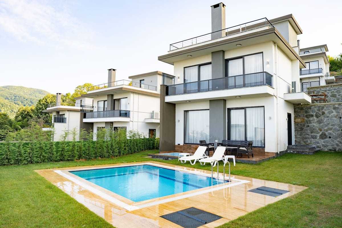 Ein modernes, mehrstöckiges Haus mit Swimmingpool, Außenbereich und einer Steinmauer.