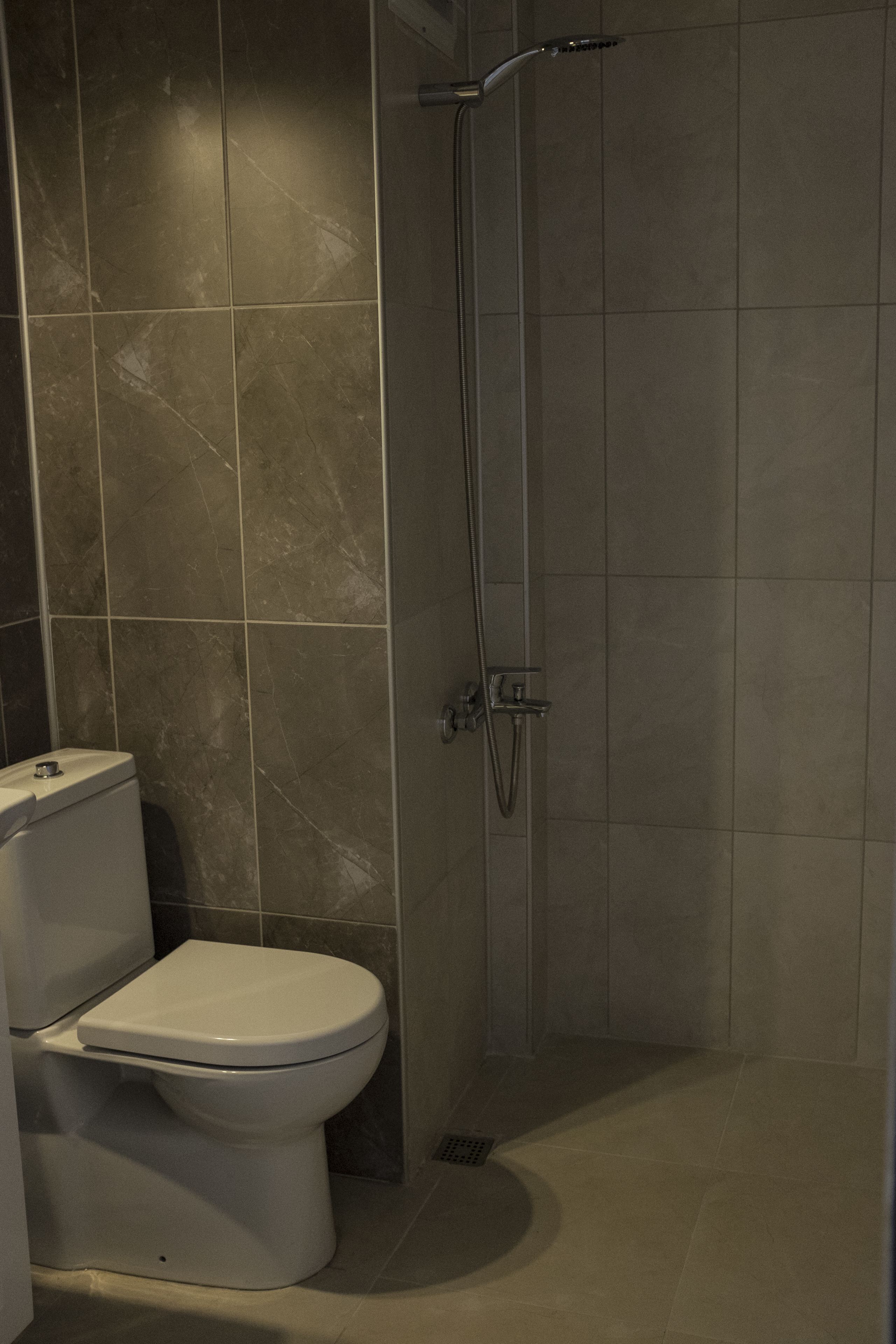 A bathroom with a toilet, a shower, and tiled walls.