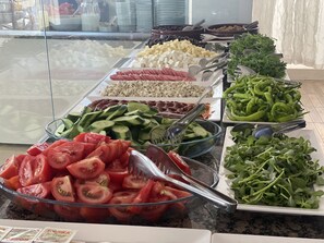 Ein reichhaltiges Buffet mit verschiedenen Speisen, darunter Gurkenscheiben, Tomaten, grüne Bohnen und Käse.