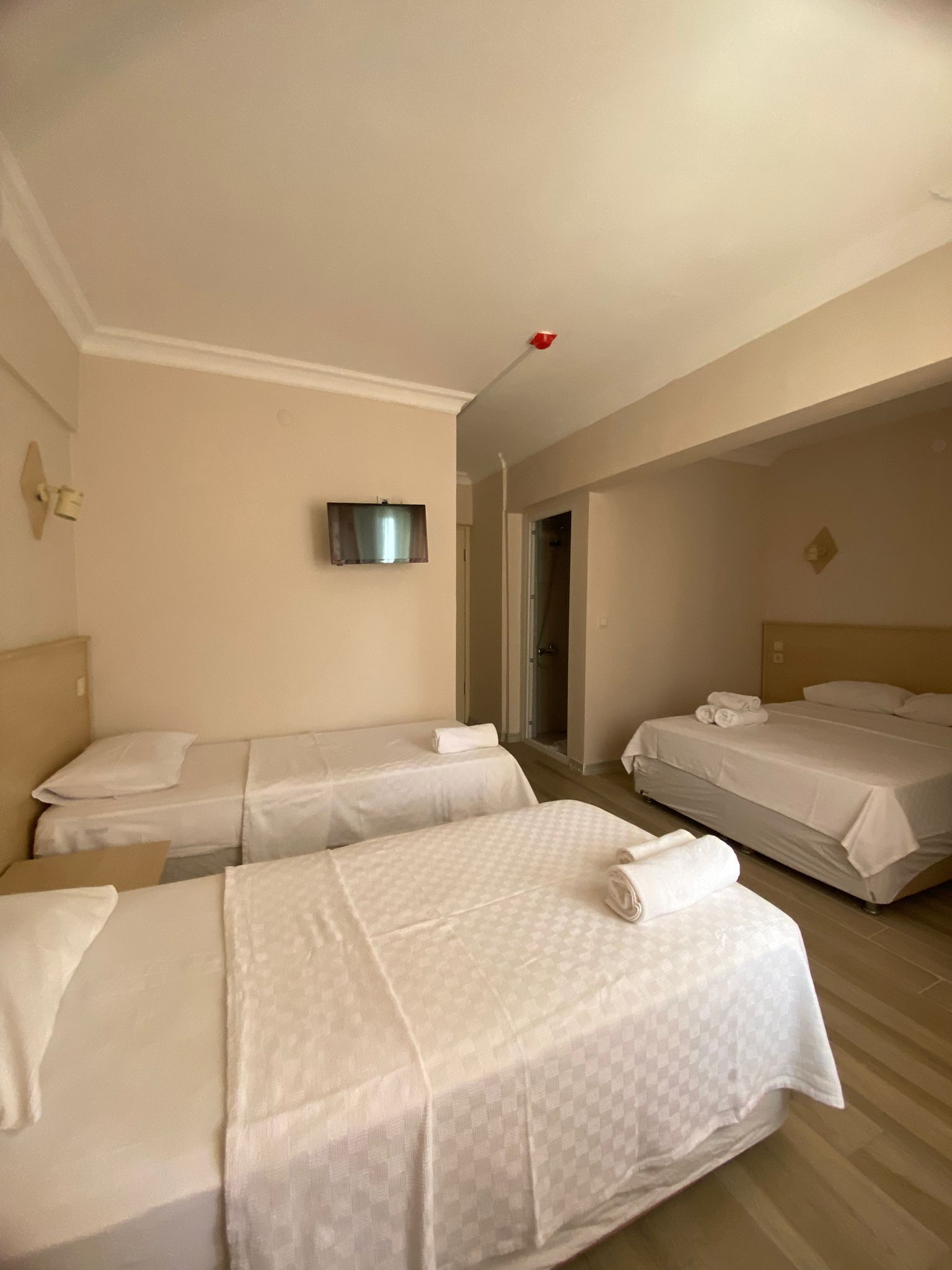 A hotel room with three beds, a TV mounted on the wall, and a red emergency light.